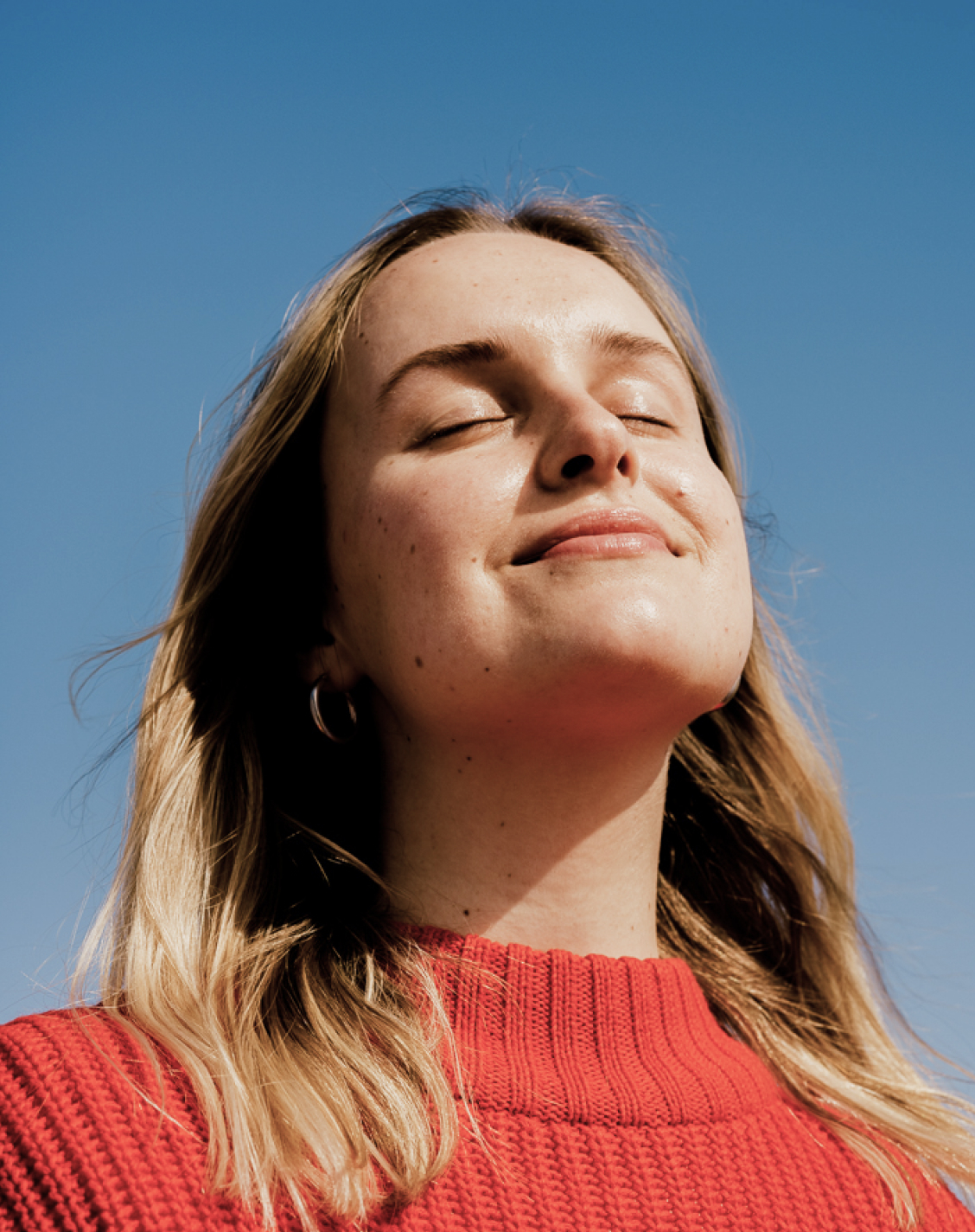 Woman smiling and tilting her head in front of a blue sky