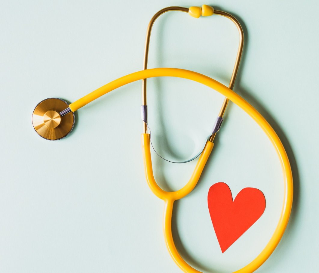 A yellow stethoscope on a green surface with a paper heart next to it