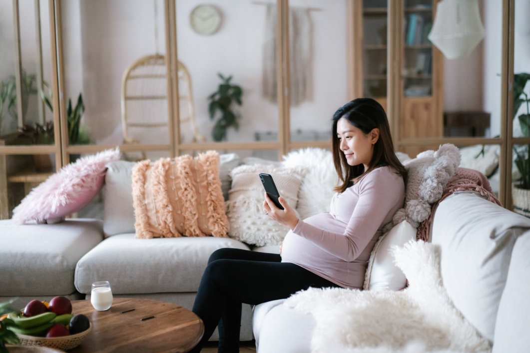 A pregnant woman sitting on a couch in her home while having a video call on her phone