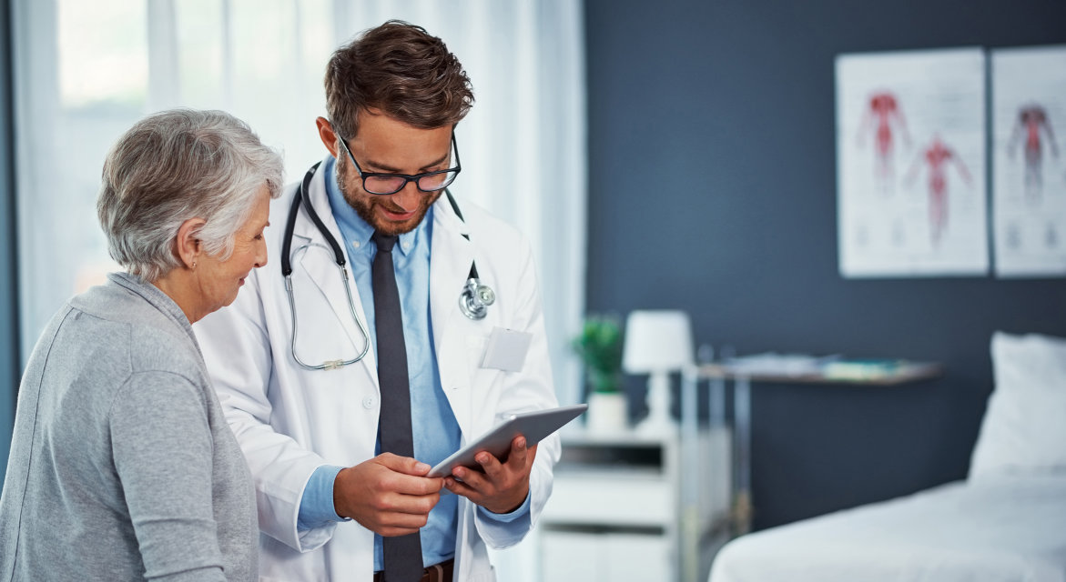 A male doctor showing an elderly female patient information on his tablet.