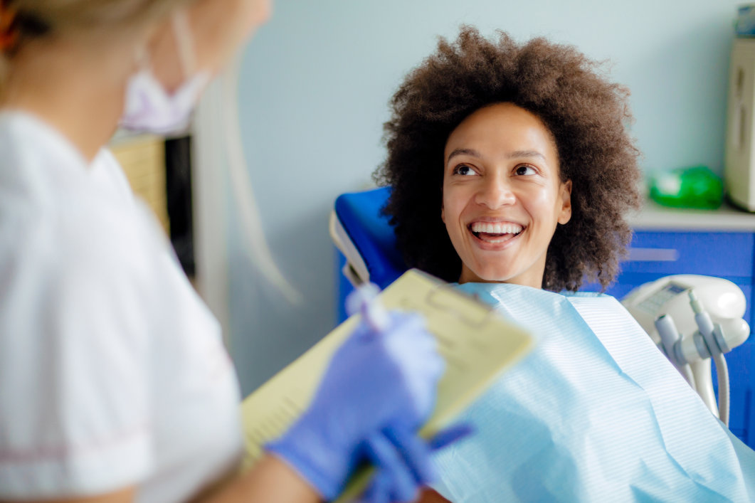 A dentist talks to a patient sitting in a chair during an appointment