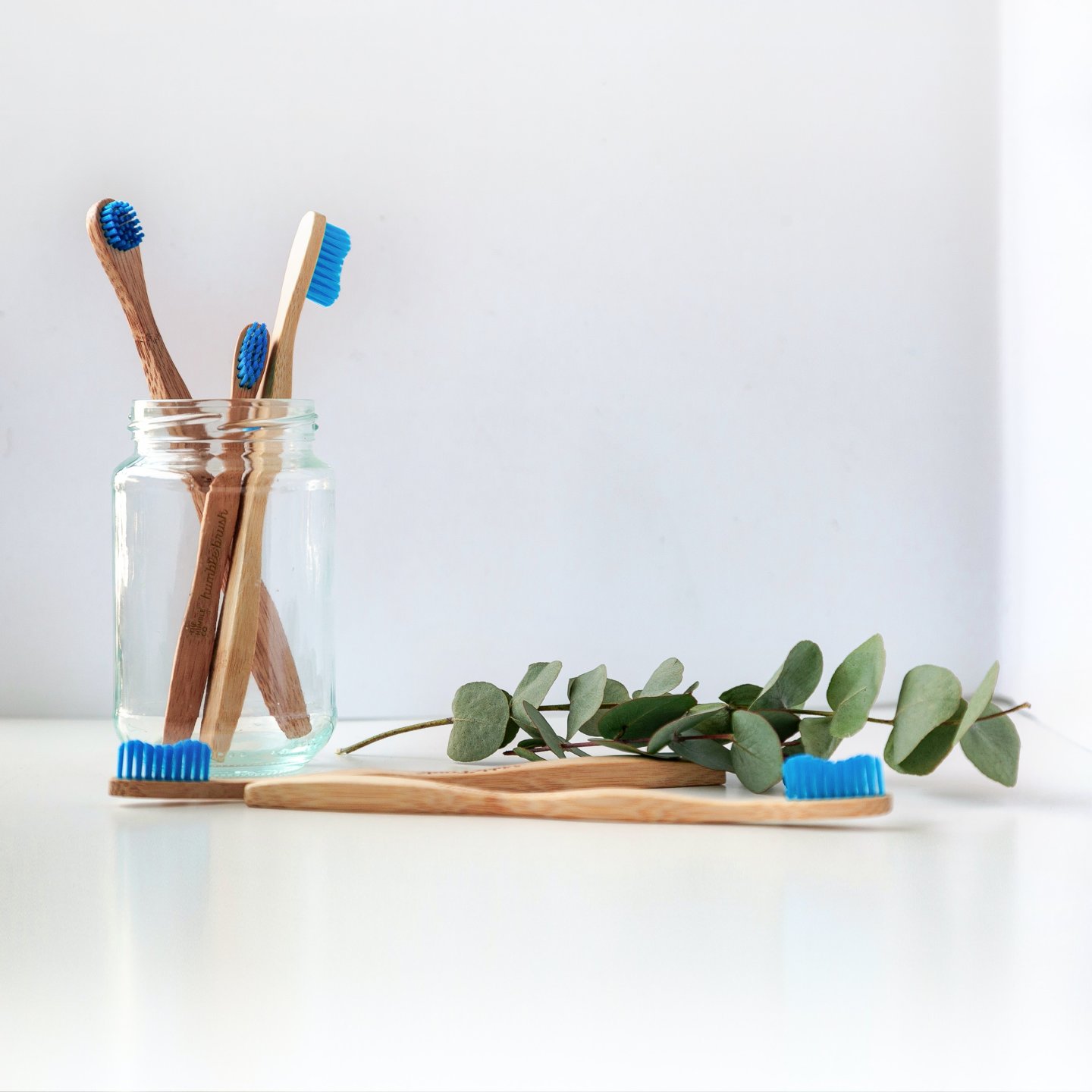 Toothbrushes with wooden handles placed in a clear jar and on the table