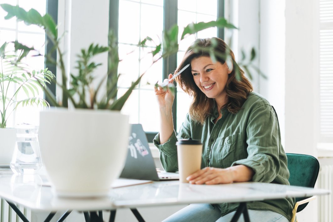 A female employee smiling while working in a bright office surrounded by plants