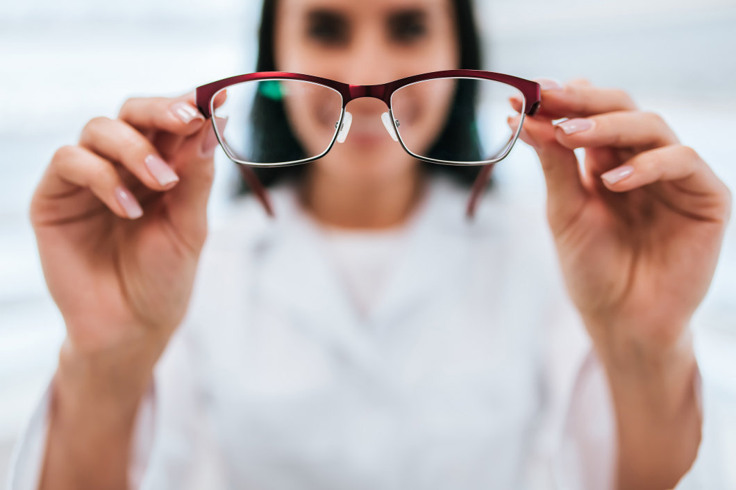 An out-of-focus image of a woman holding up eyeglasses that are in focus.