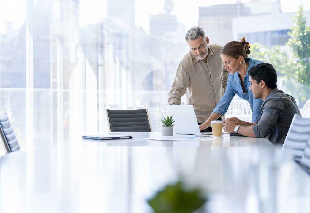 Three colleagues together in an office meeting room looking at a laptop screen