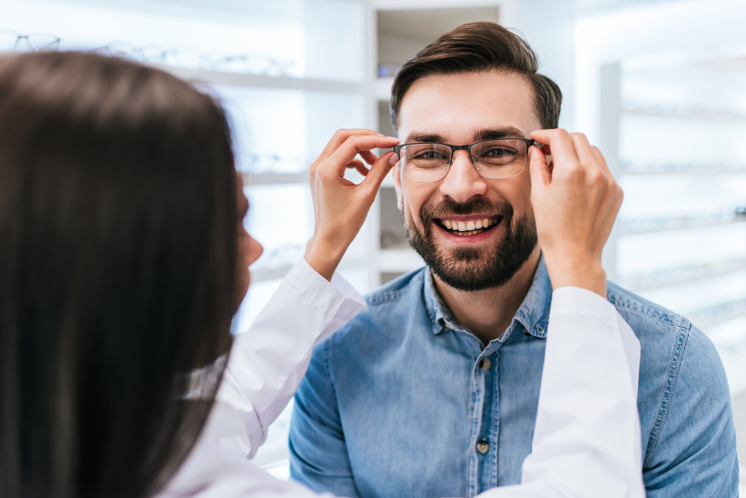 A female doctor helping a male patient try on a pair of glasses.