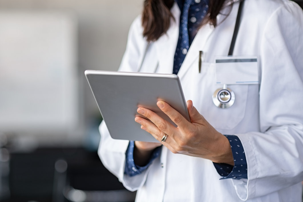 A female doctor holding and reading a tablet that contains a medical report.