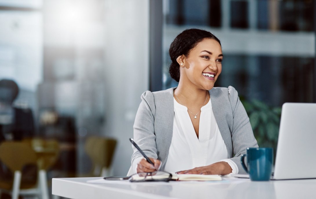 A business woman smiling at her desk while writing down ideas