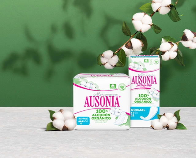 Dos paquetes: las compresas y protegeslips Ausonia Cotton Protection. Están rodeados de flores de algodón.