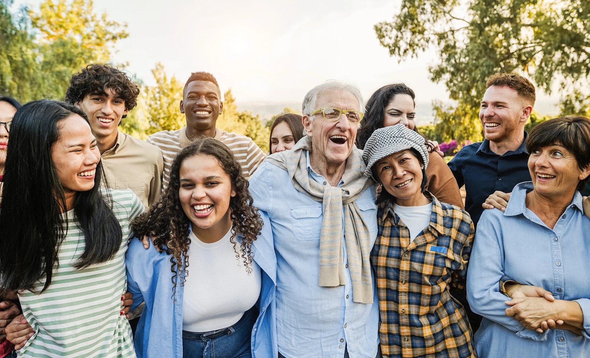 A group of young and older people from various backgrounds hug each other and laugh.