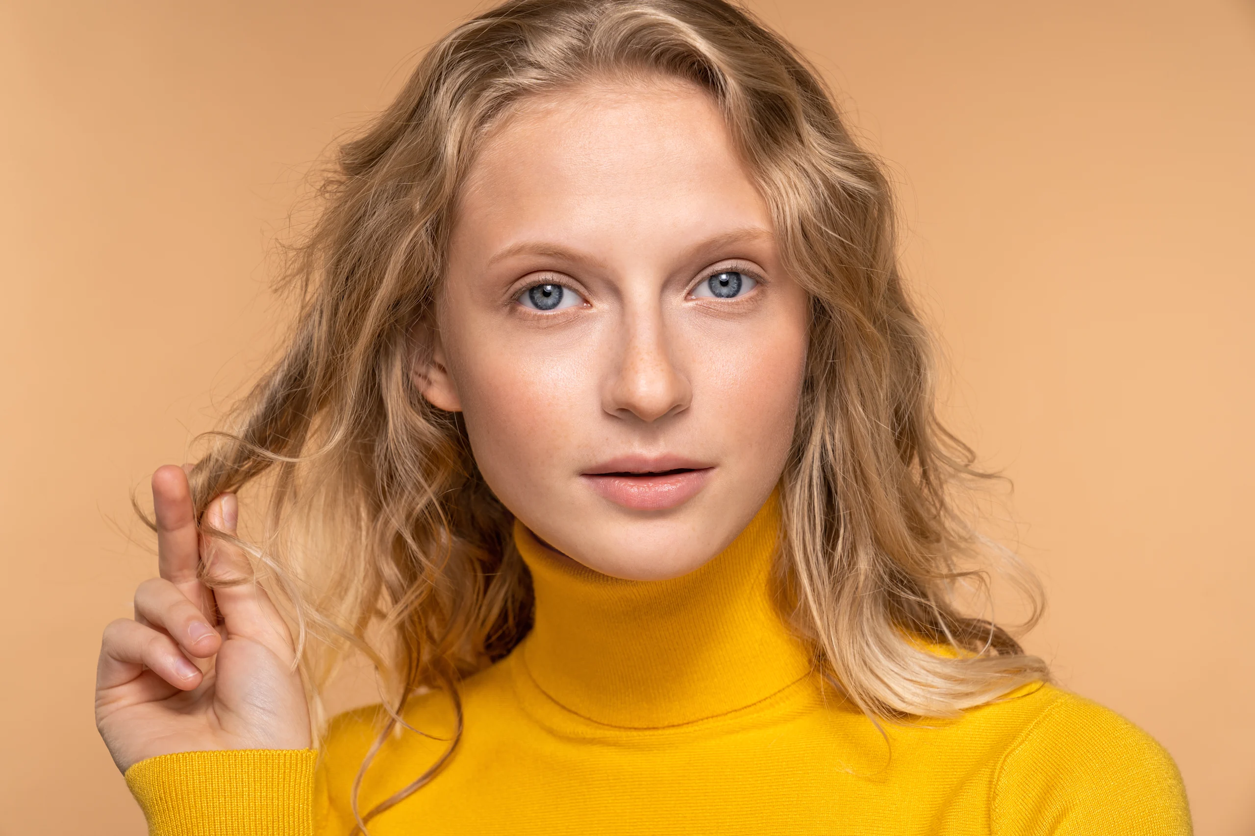 Luonnollisesti meikattu nainen katsoo kameraan, päällään keltainen poolopaita