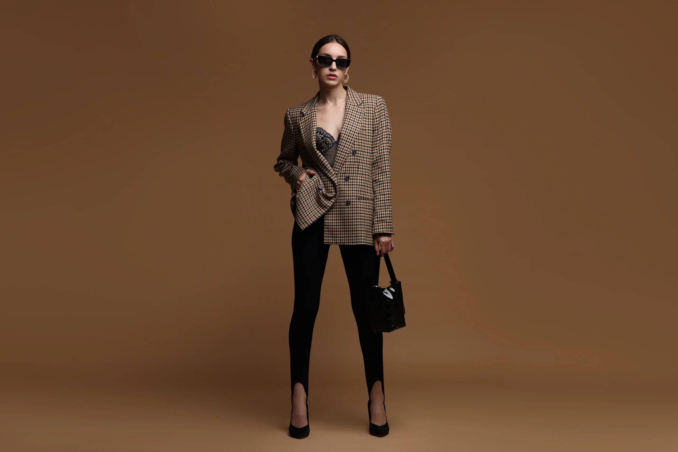 Tyylikkäästi pukeutunut nainen poseeraa ruskeaa taustaa vasten