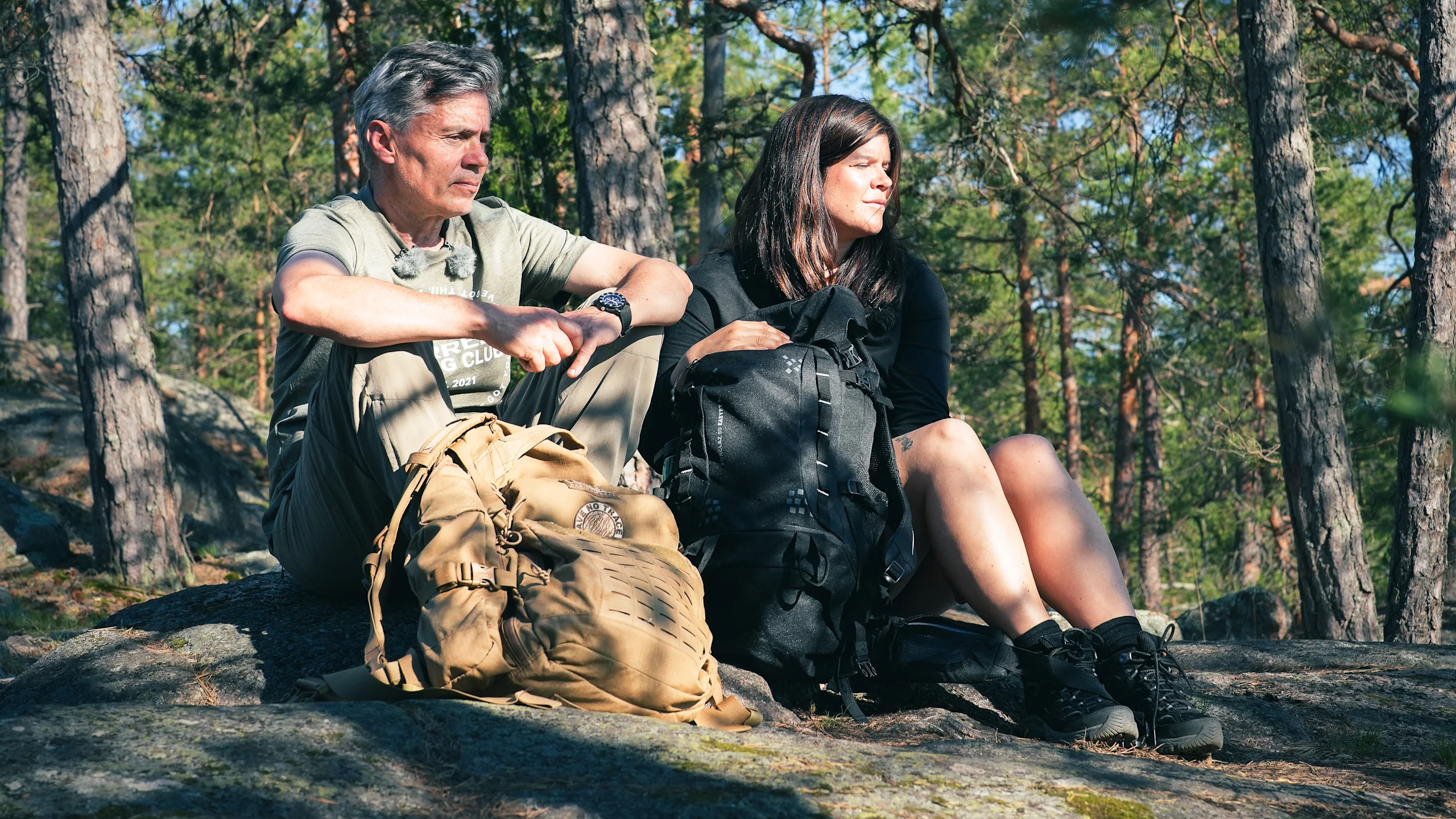 Jukka Viljanen ja Mirka Nyqvist istuvat kalliolla Nuuksiossa. Aurinko paistaa puiden lomasta.