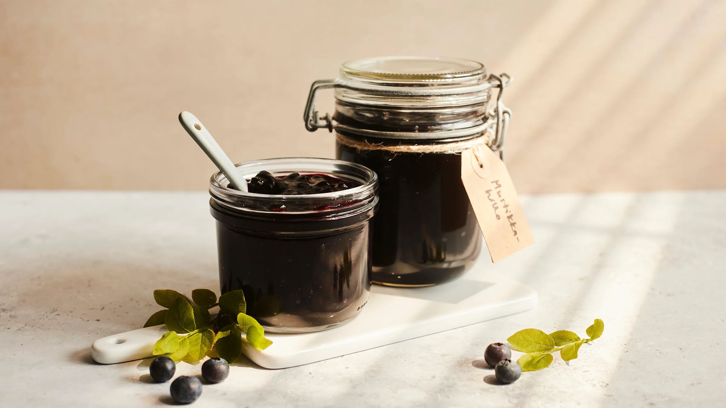 Mustikkahilloa lasipurkeissa, pöydällä muutama mustikanvarpu