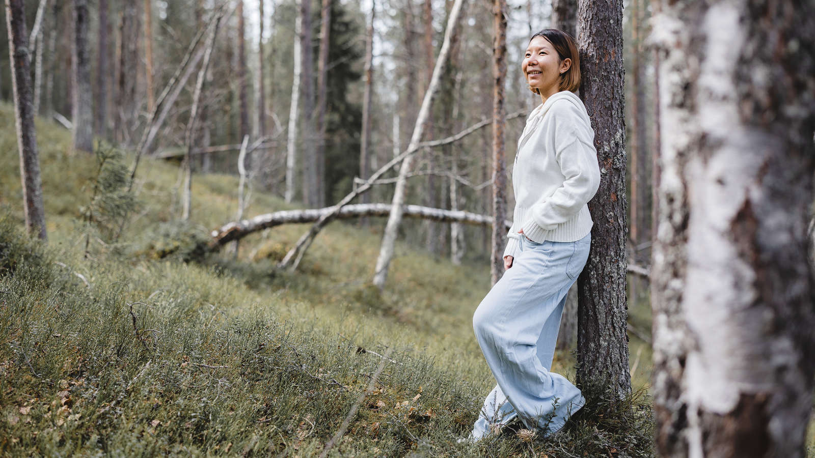 Nainen nojaa metsässä puuhun