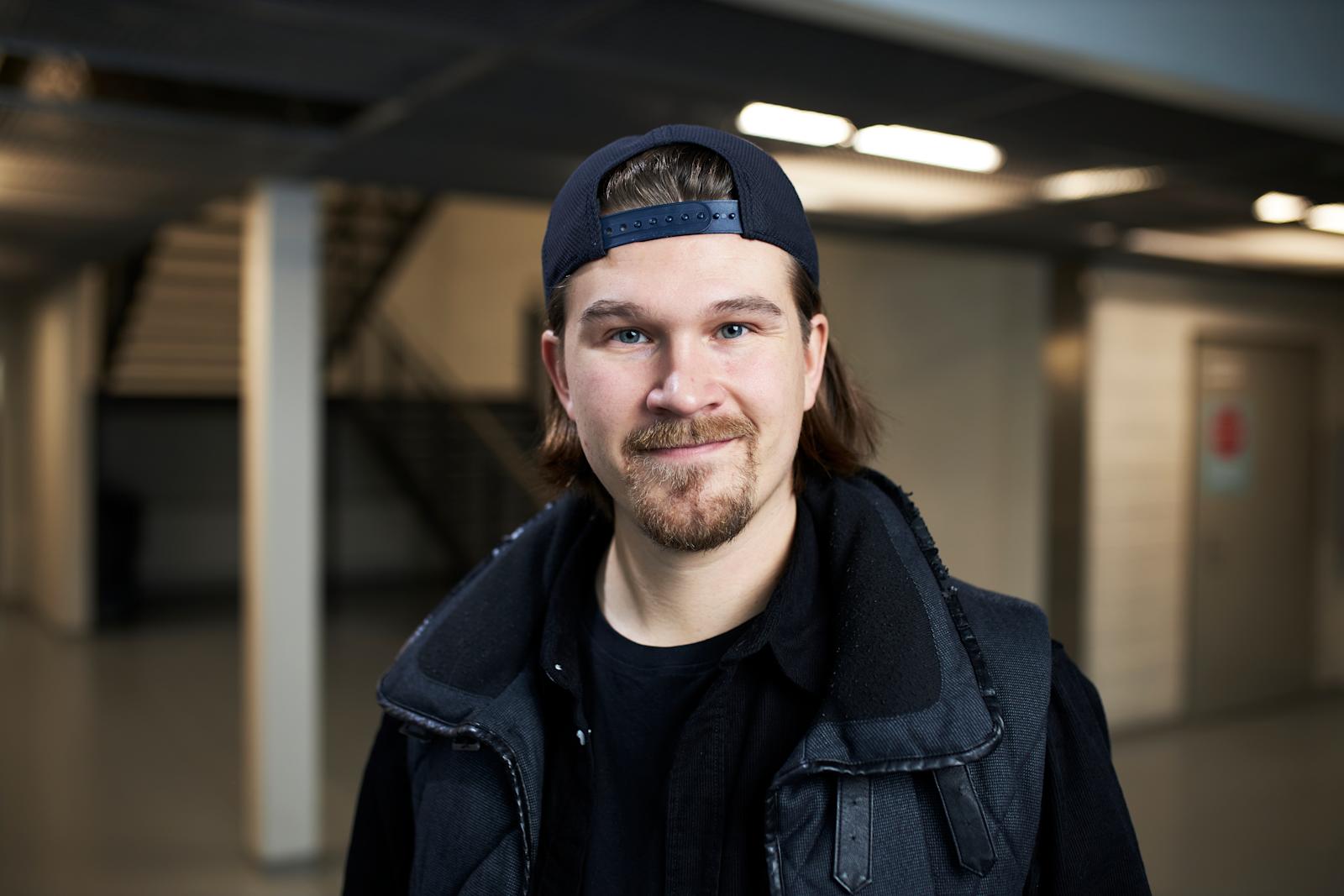 Eetu Patronen katsoo kameraan. Hänellä on lippis väärinpäin päässä ja päällään tumma takki.