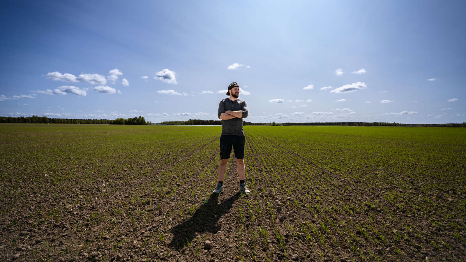 Antti Kartano seisomassa pellon keskellä hymyillen, kädet puuskassa.