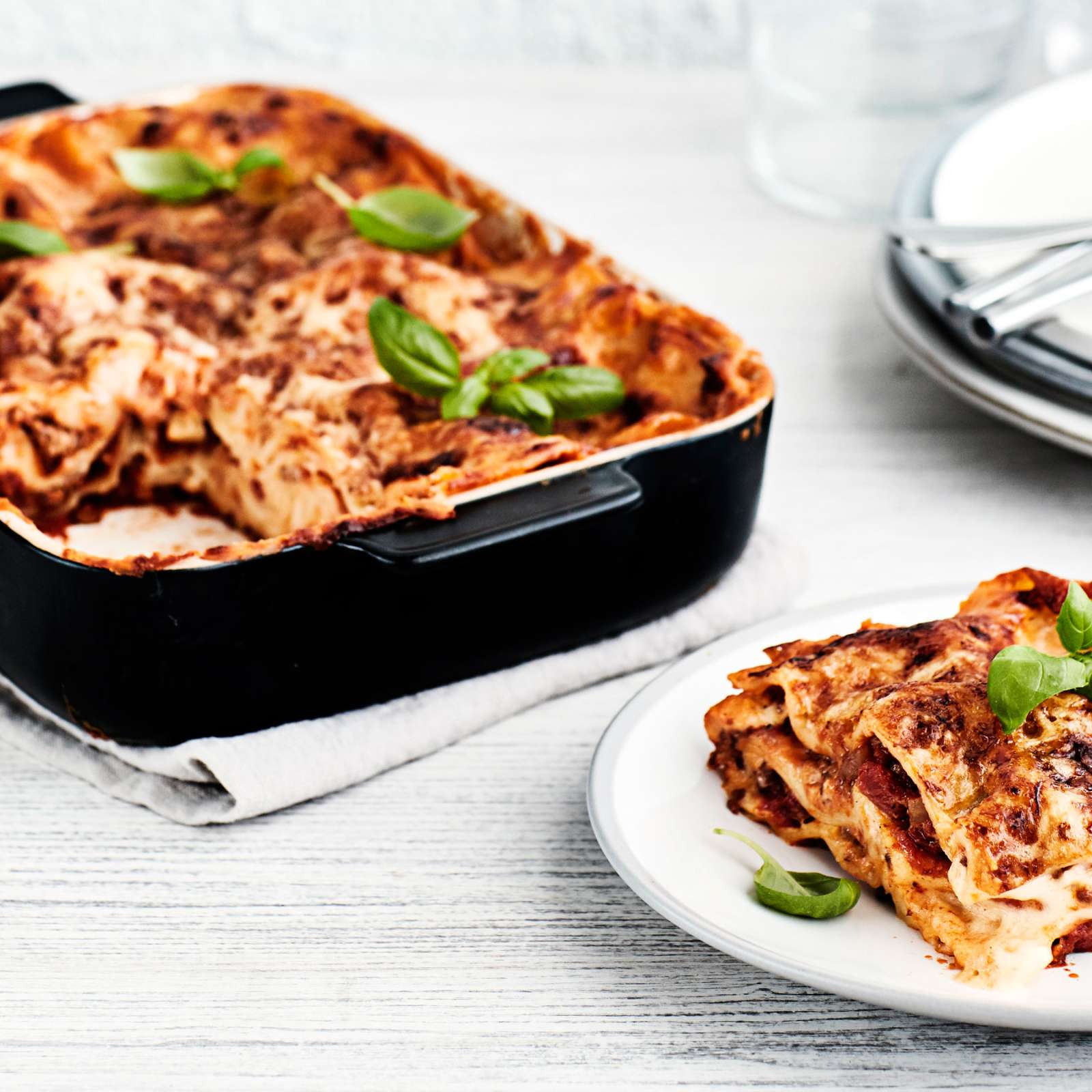 Lasagne mustassa uunivuoassa ja lautanen, jonka päällä basilikan lehdillä koristeltu annos lasagnea.