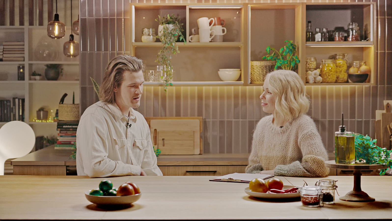 Eetu Patronen Ässästudion keittiössä toimittaja Minna Perovuon haastateltavana. Pöydällä hedelmiä. Taustalla hyllyjä, joissa muun muassa kahvikuppeja, kippoja, mausteita ja lasipurnukoita.