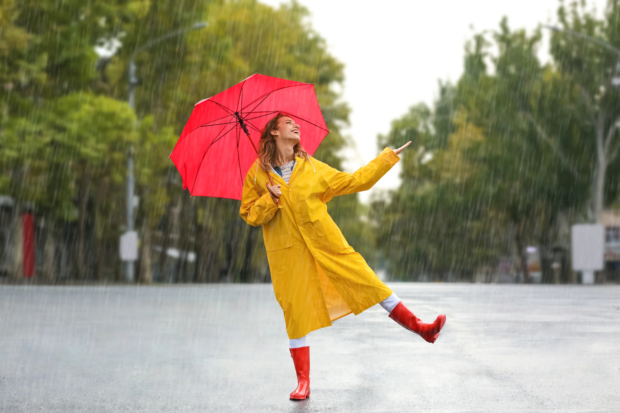 Keltaiseen sadetakkiin pukeutunut, hyväntuulinen nainen punaisen sateenvarjon alla