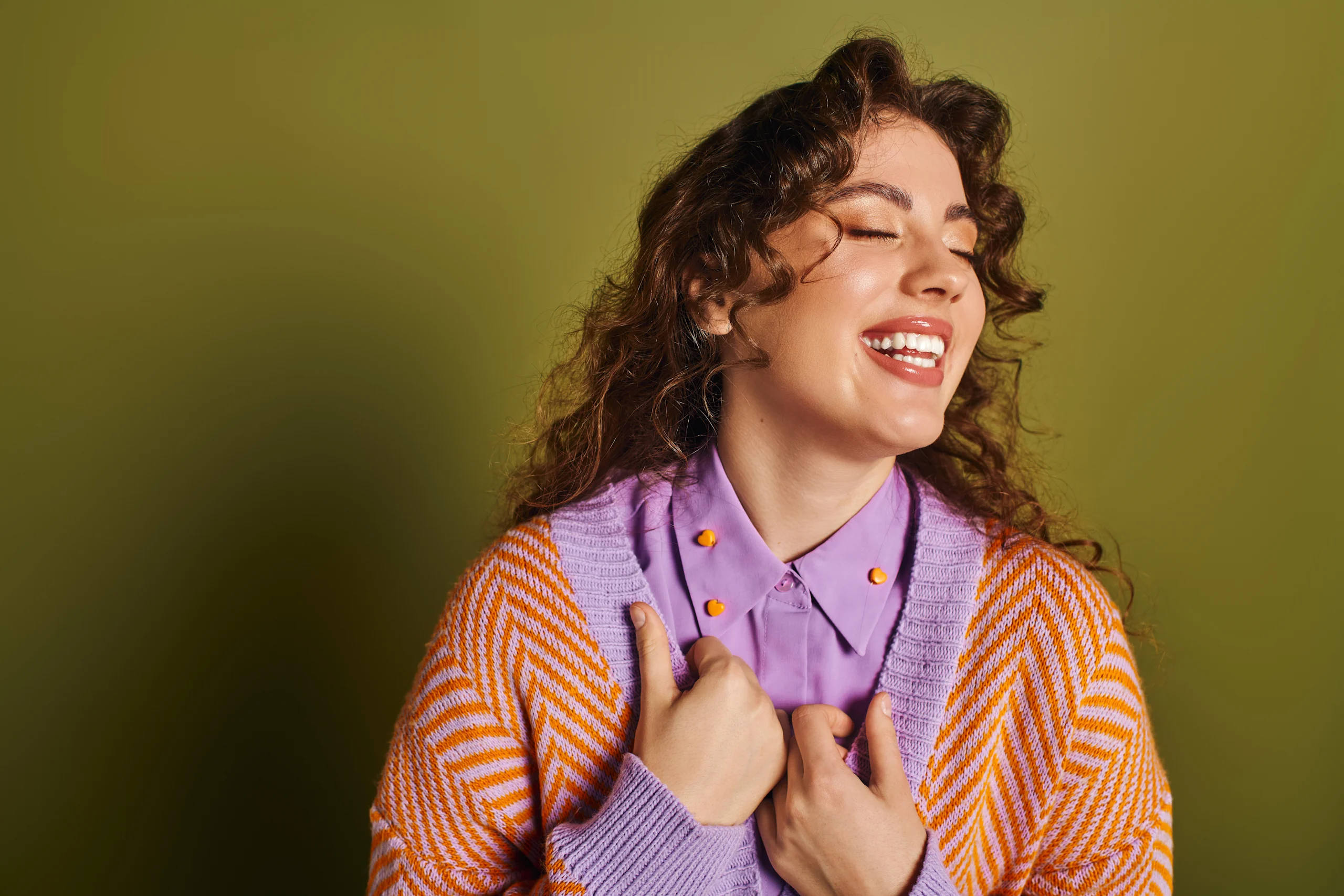 Hymyilevä kiharahiuksinen nainen poseeraa vihreää taustaa vasten