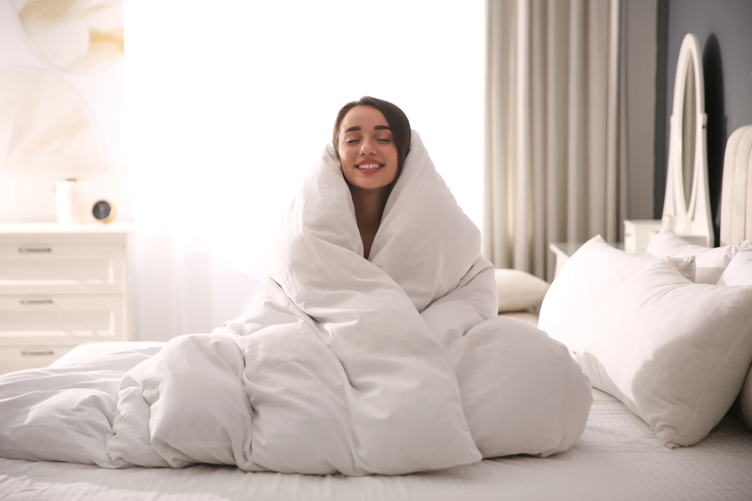 Iloinen nainen sängyssä peittoon kääriytyneenä