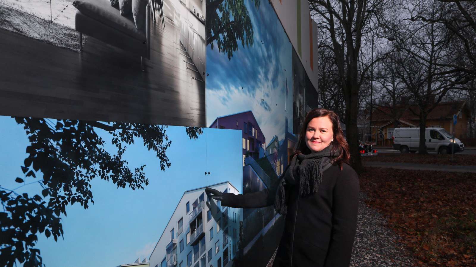 Elina Martikainen seisoo pihalla asuntoja mainostavan näyteikkunan edessä. 