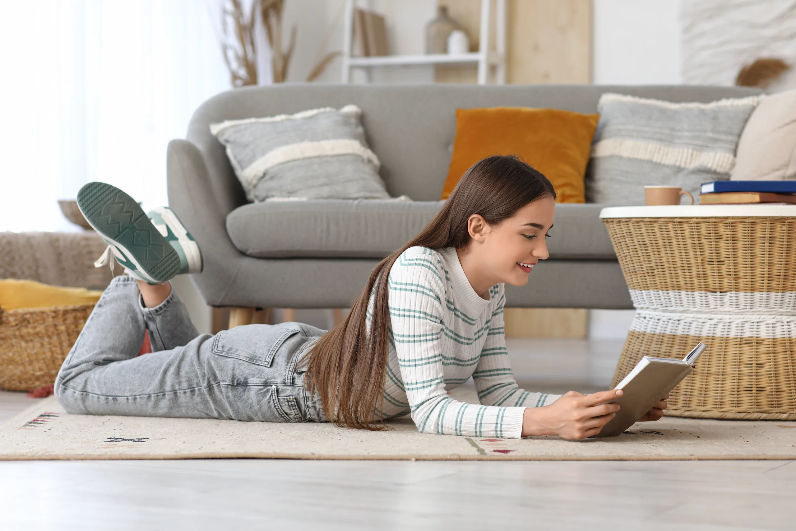 Nainen makaa lattialla vatsallaan ja lukee kirjaa