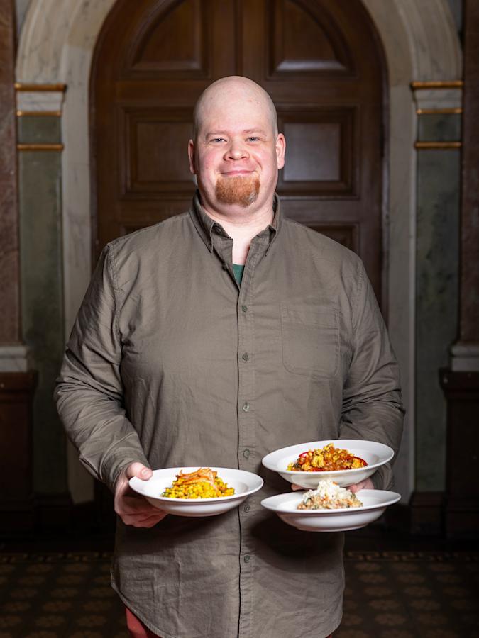 Lauri Hakala pitelee kolmea syvää lautasta, jotka sisältävät kolmea eri ruokaa. Laurilla on päällään kauluspaita.