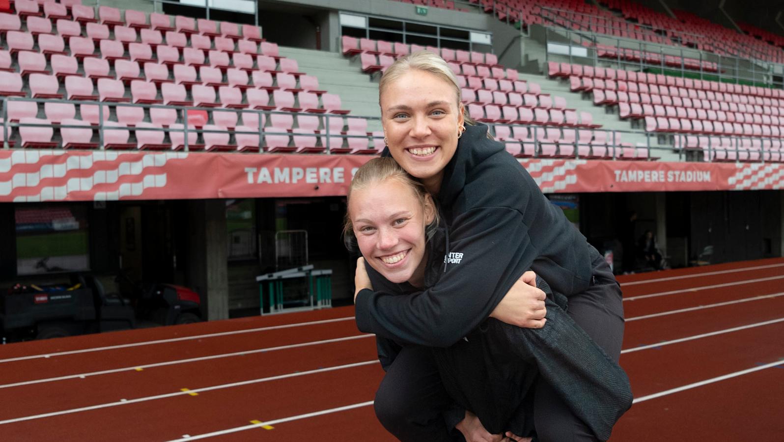 Yleisurheilijat Saga Vanninen ja Vilma Itälinna Tampereen Ratinan stadionilla. Saga kantaa Vilmaa reppuselässä.