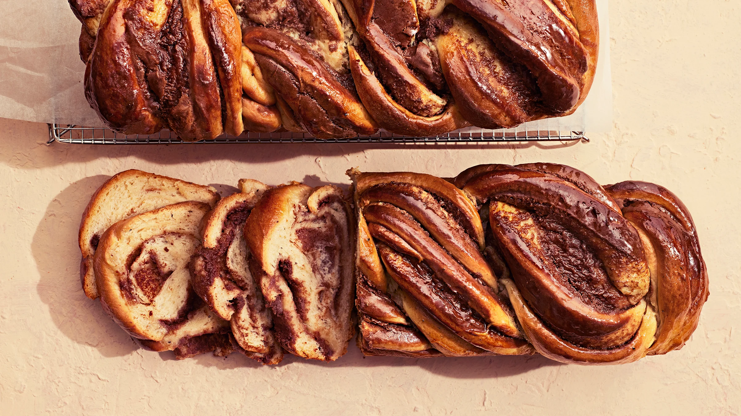 Suklainen pullapitko, josta leikattu neljä viipaletta. Vieressä kokonainen pitko leivinpaperoidun ritilän päällä.