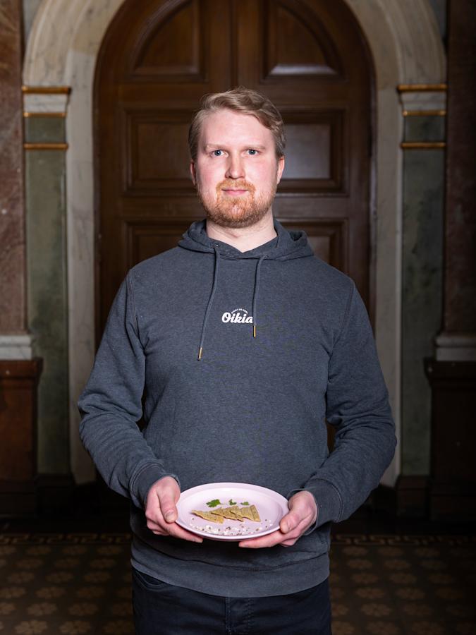Topias Kinnusella on päällään harmaa huppari. Kädessä lautanen, jolla hän pitelee tuomaristolle esittelemäänsä tuotetta.