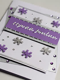 **Lumihiutaleet**: Liimaa korttipohjalle hopea ja violetti kartonkiraita. Leikkaa kuvioleikkurilla lumihiutaleita. Käytä myös tarroja.
