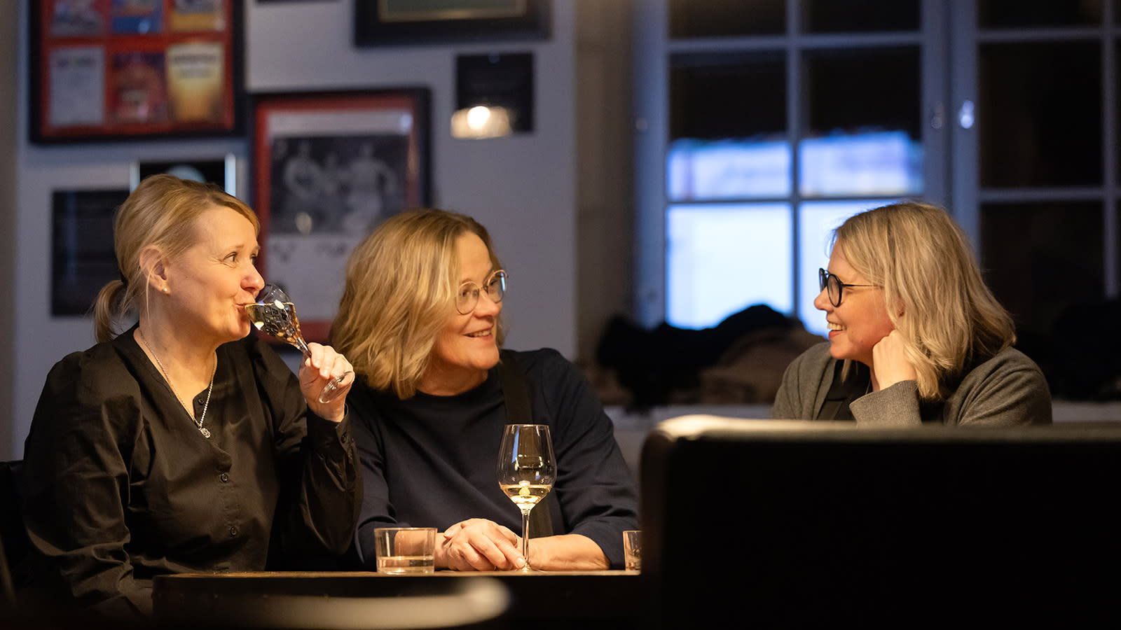 Anne Rajasalo, Arja Eränen ja Arja Salokangas keskustelevat ravintolan pöydän äärellä laseissaan juomaa.