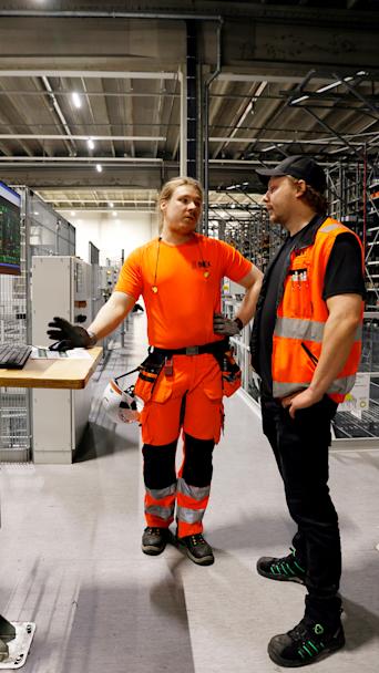 Kaksi työasuun pukeutunutta miestä juttelee logistiikkakeskuksessa