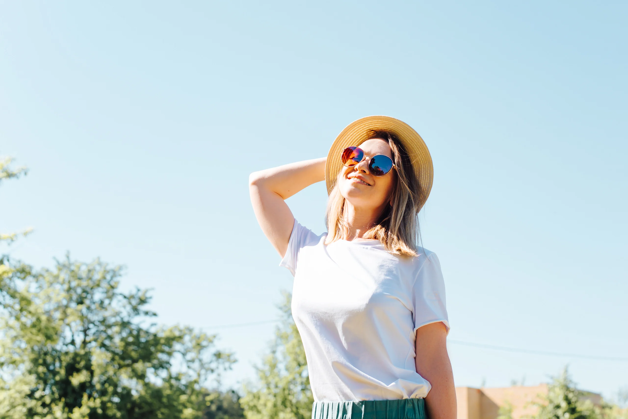 Hymyilevä nainen poseeraa valkoisessa t-paidassa ja aurinkolaseissa