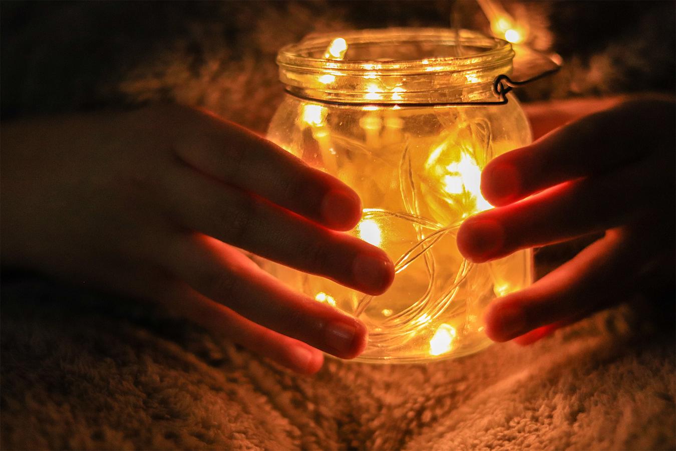 Kädet valaistun lasipurkin ympärillä.