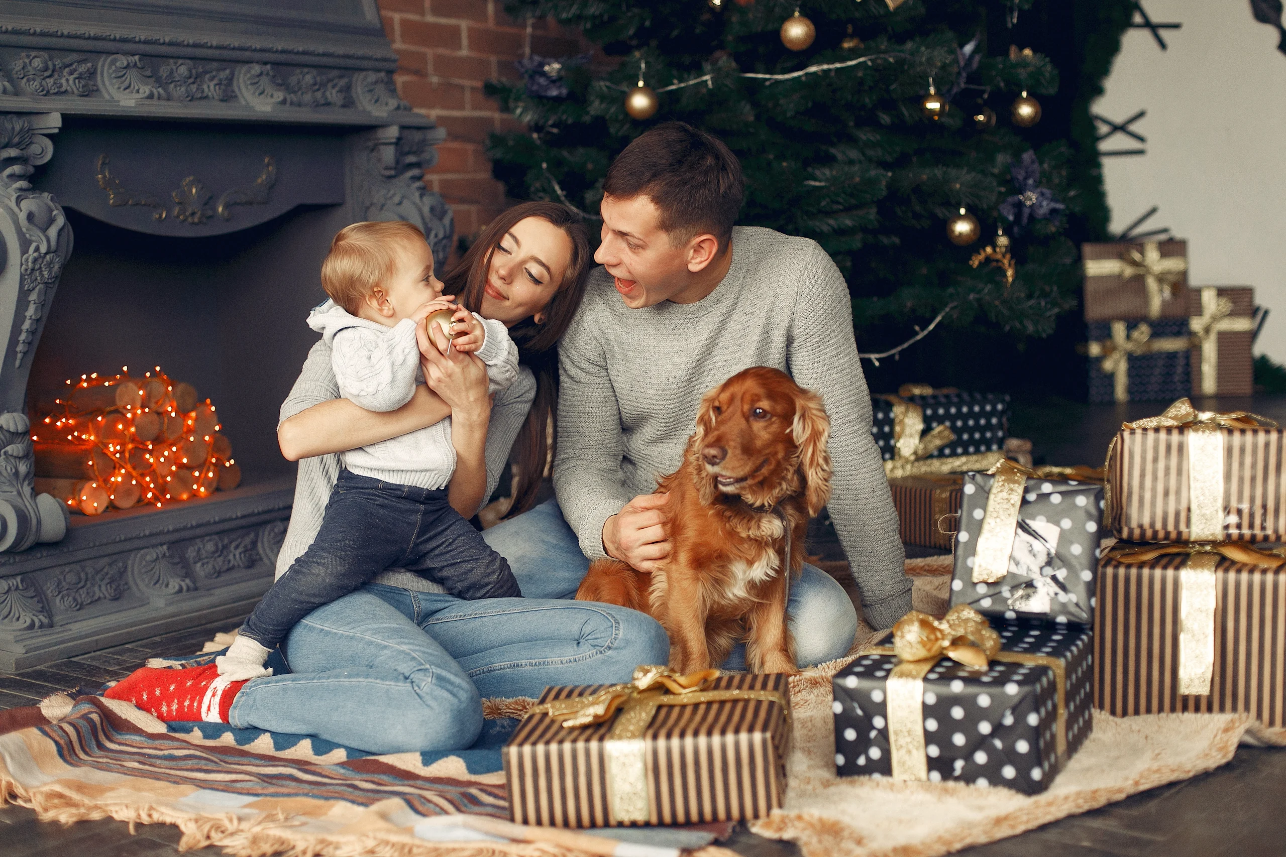 Perhe ja perheen koira joulukuusen äärellä, lattialla runsaasti lahjoja