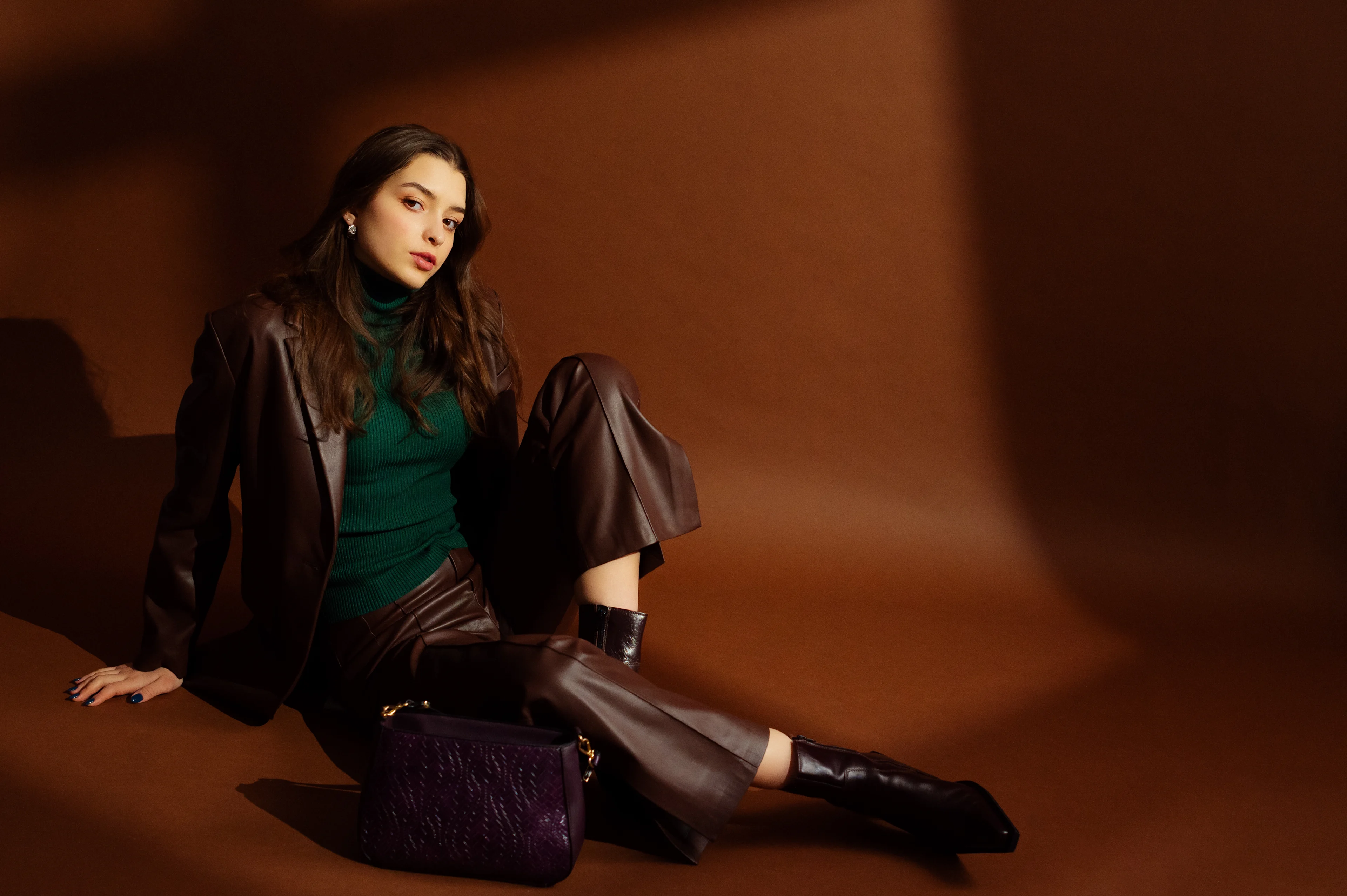 Suklaanruskeaan asuun pukeutunut nainen poseeraa lattialla rennosti istuen