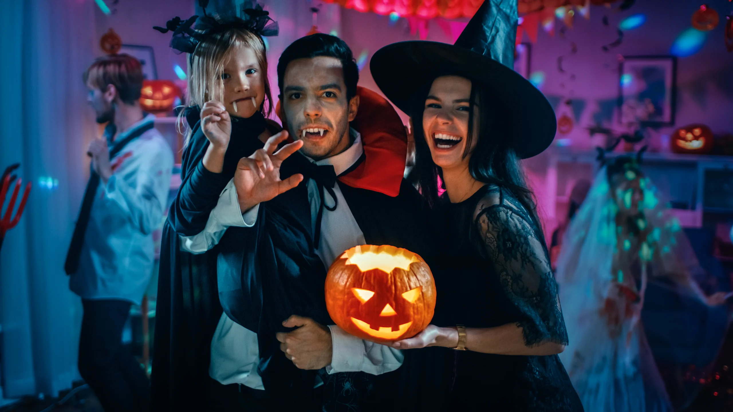 Vampyyriksi pukeutuneet mies ja lapsi sekä noidaksi pukeutunut nainen Halloween-juhlissa