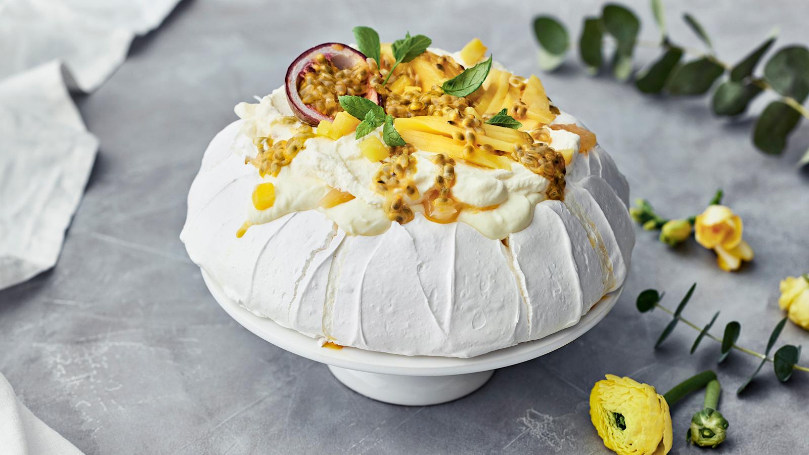 Pavlova joka on koristeltu passionhedelmällä, mangolla ja mintunlehdillä.