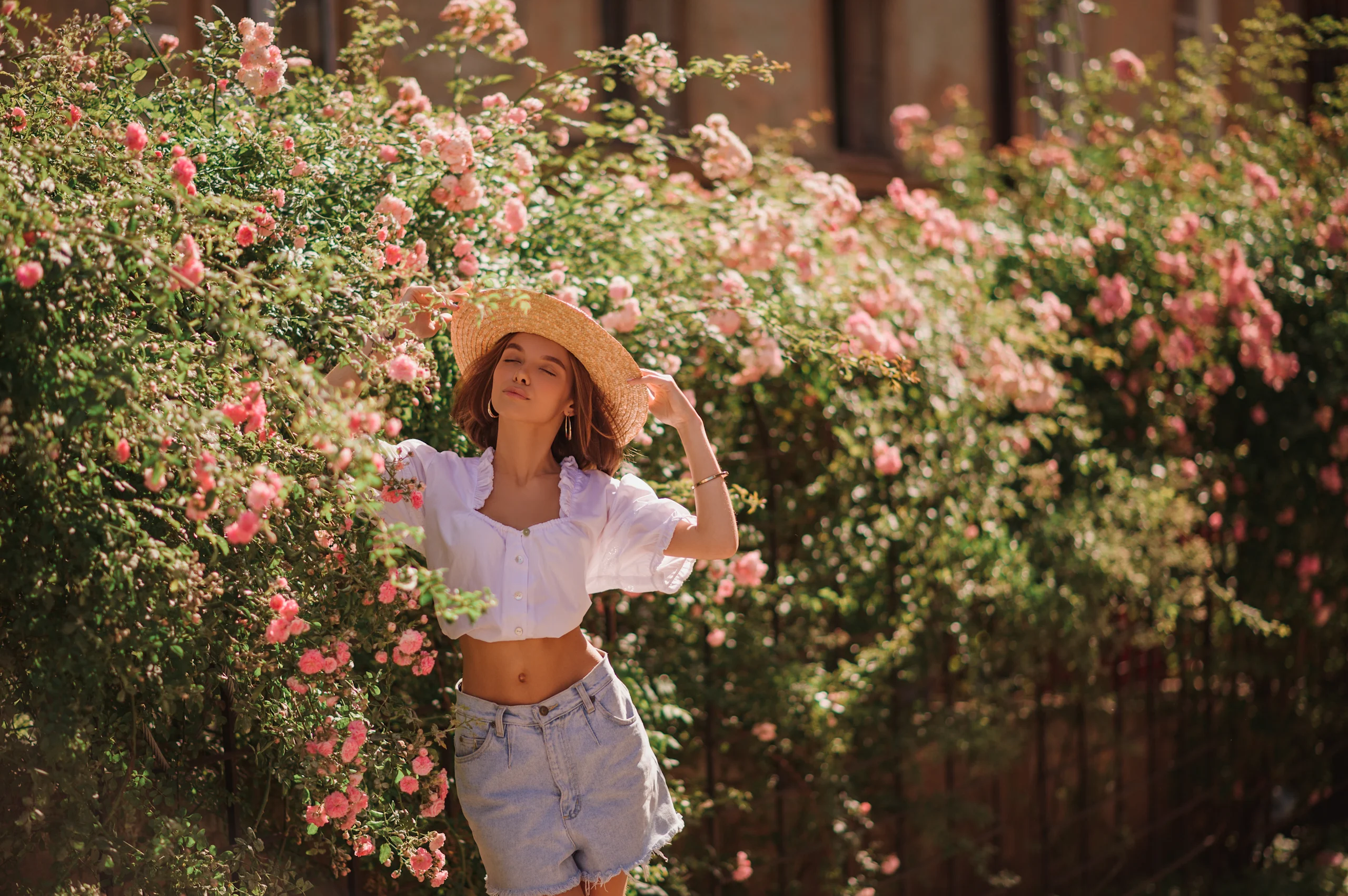 Nainen poseeraa kesäisessä asussa taustallaan kukkapuskia