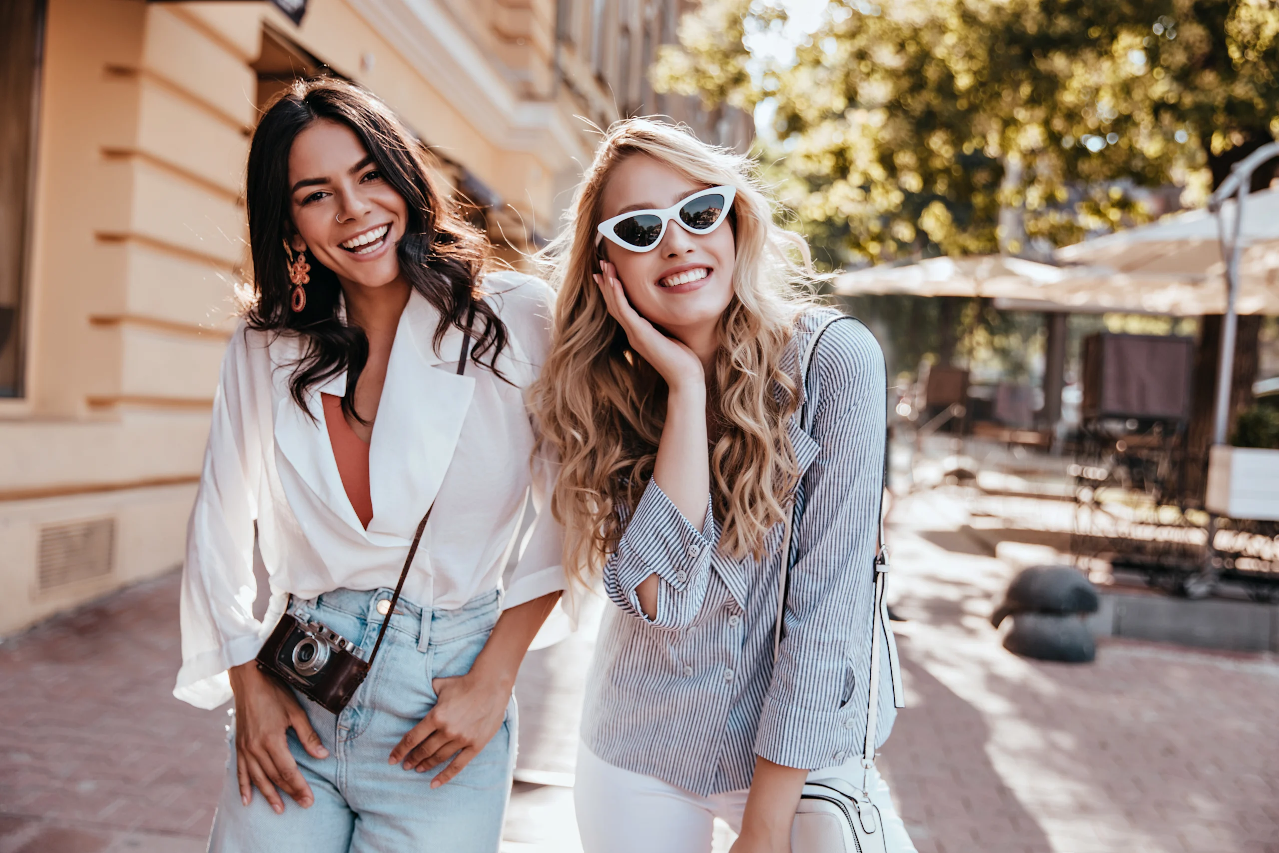 Kaksi iloista naista kaupungilla, poseeraavat kameraan katsoen