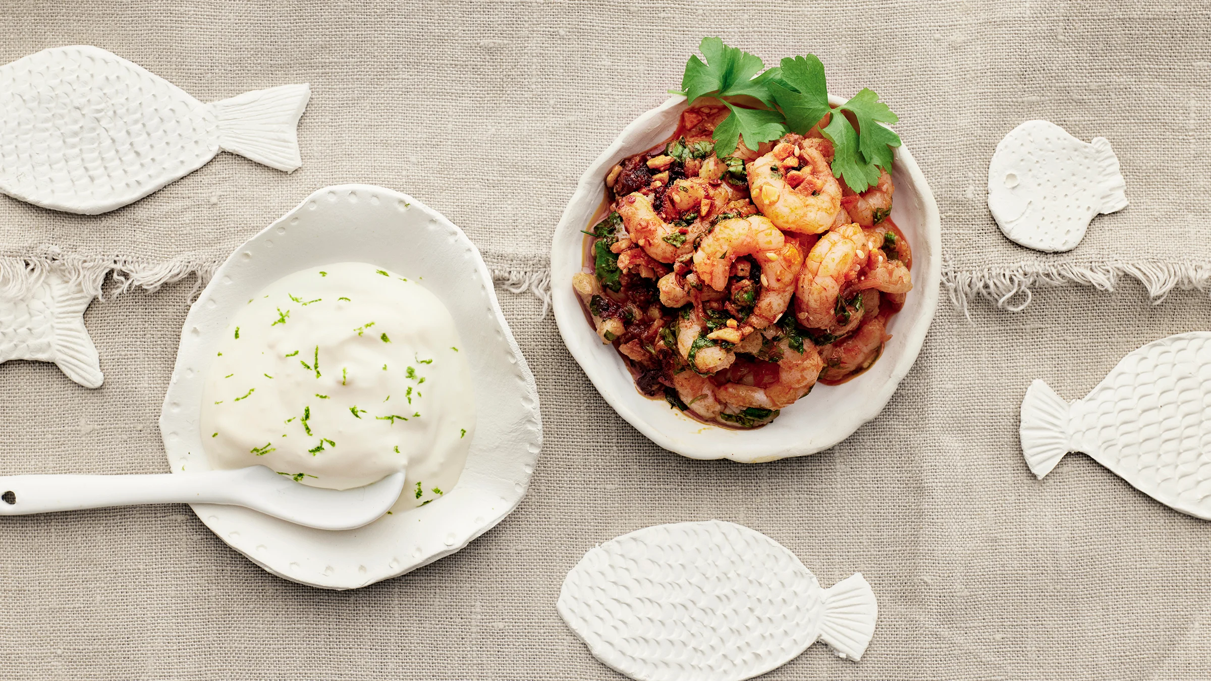 Valkosipuli-chilirapuja kulhossa korianterilla koristeltuna. Vieressä limeaiolia kulhossa, jossa lusikka.