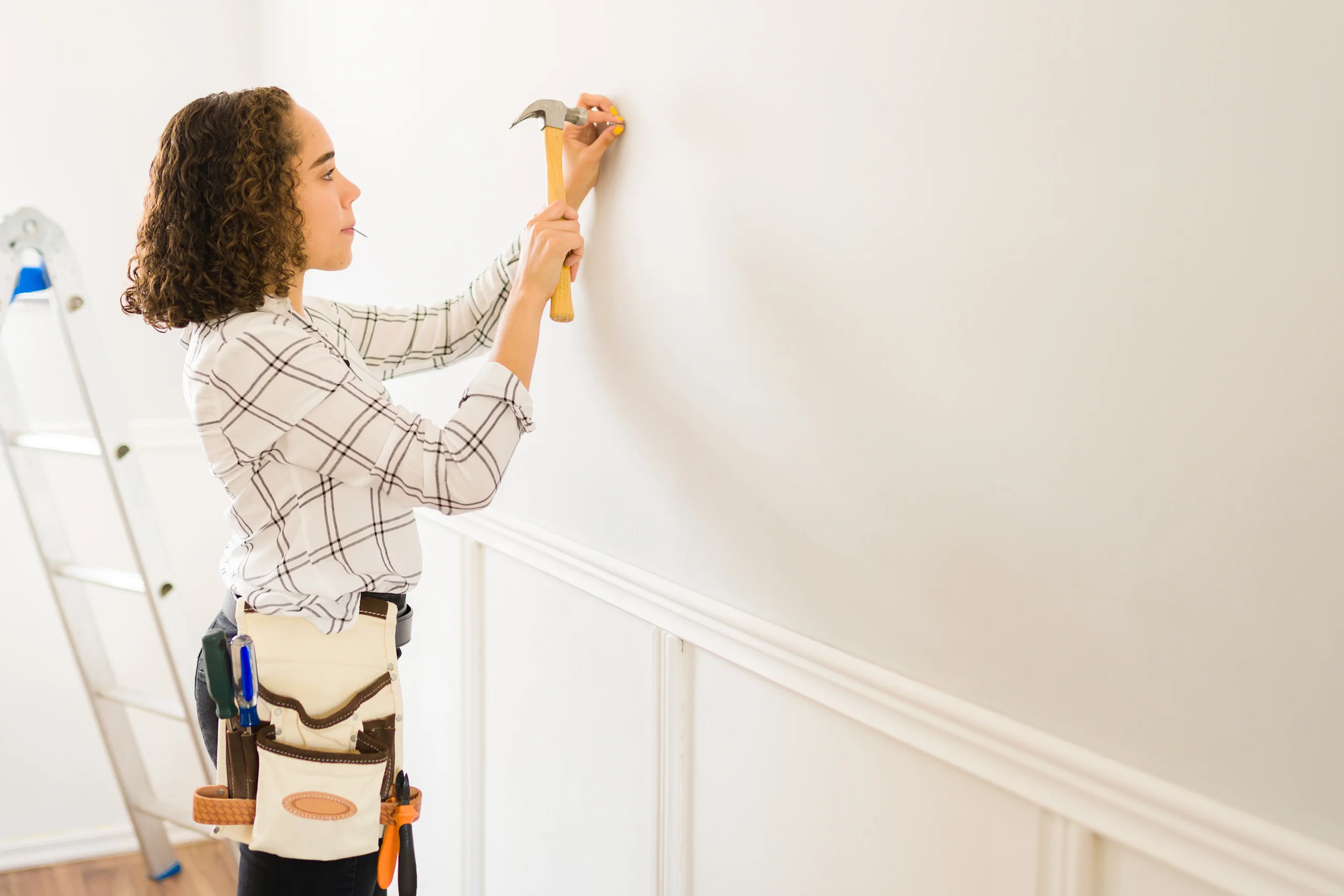 Nainen naulaa vasaralla naulaa seinään kiinni