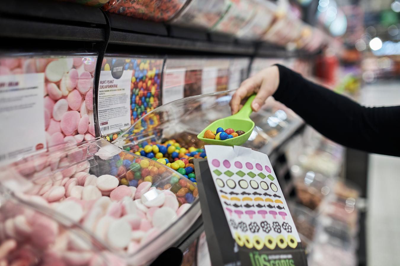Henkilö ottamassa kauhalla irtokarkkeja paperiseen irtokarkkipussiin.