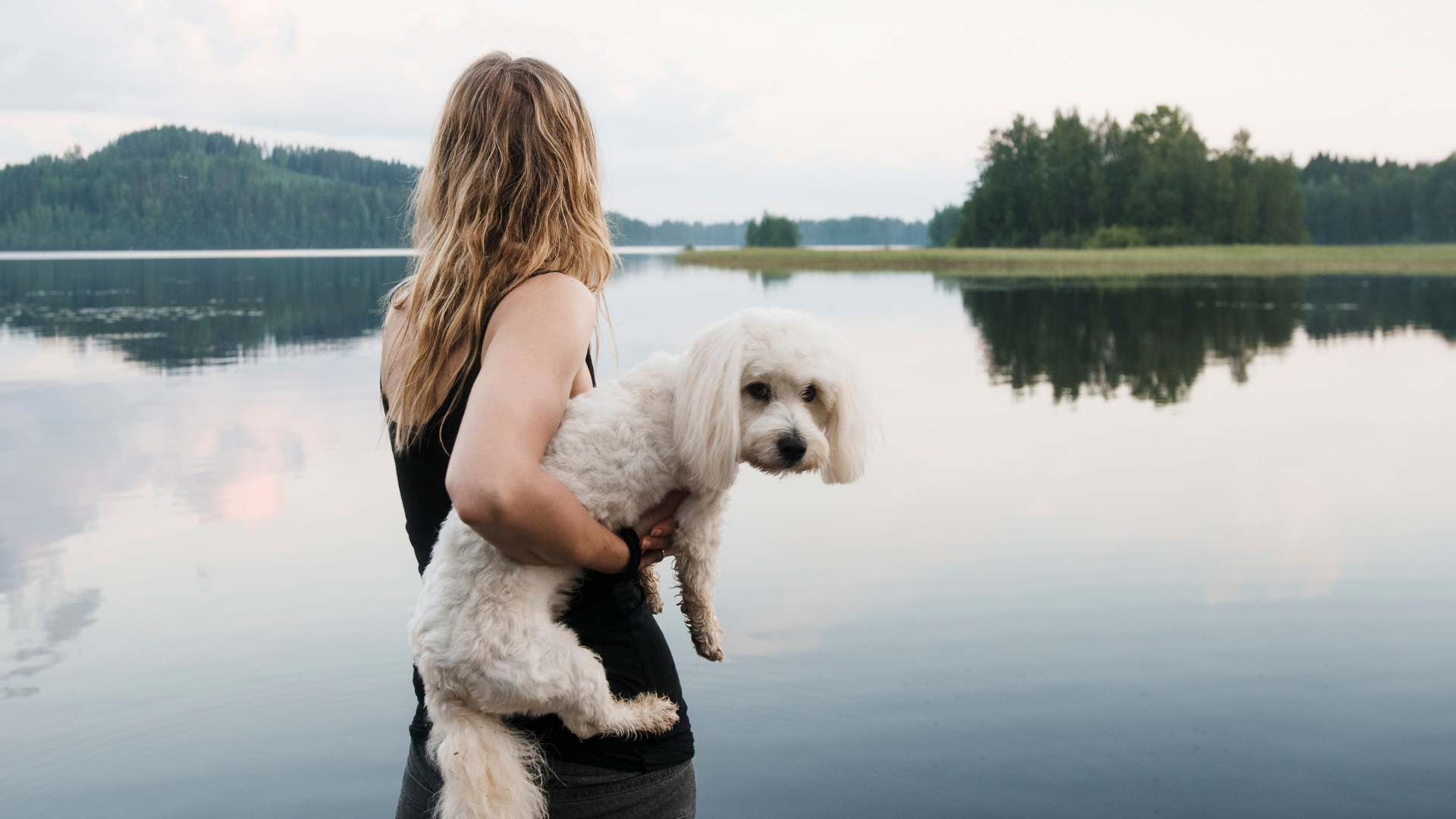 Nainen lemmikkikoiransa kanssa järven rannalla.