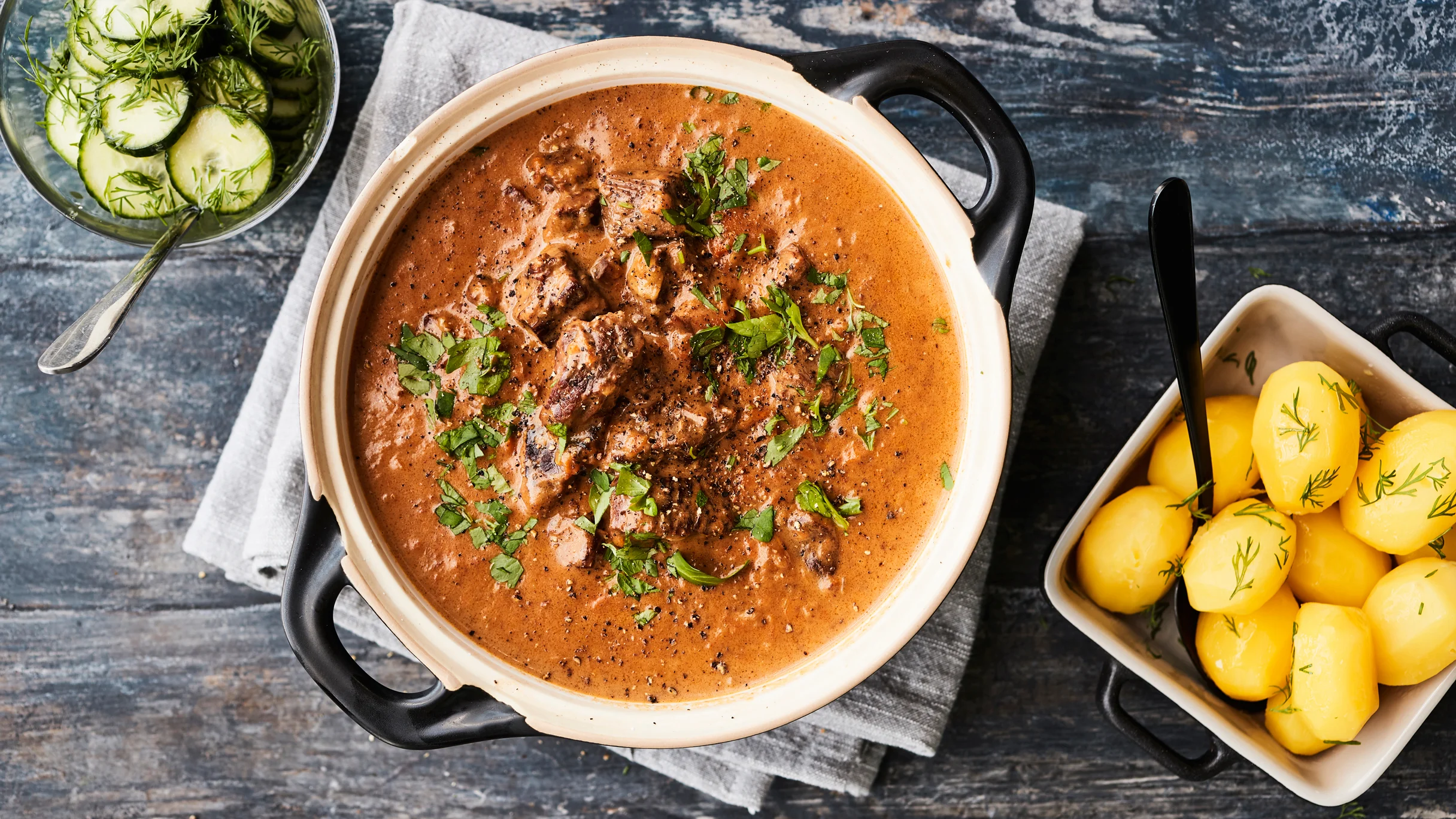 Palapaisti padassa. Vieressä keitettyjä perunoita ja hölskytyskurkkuja tarjoiluastioissa.