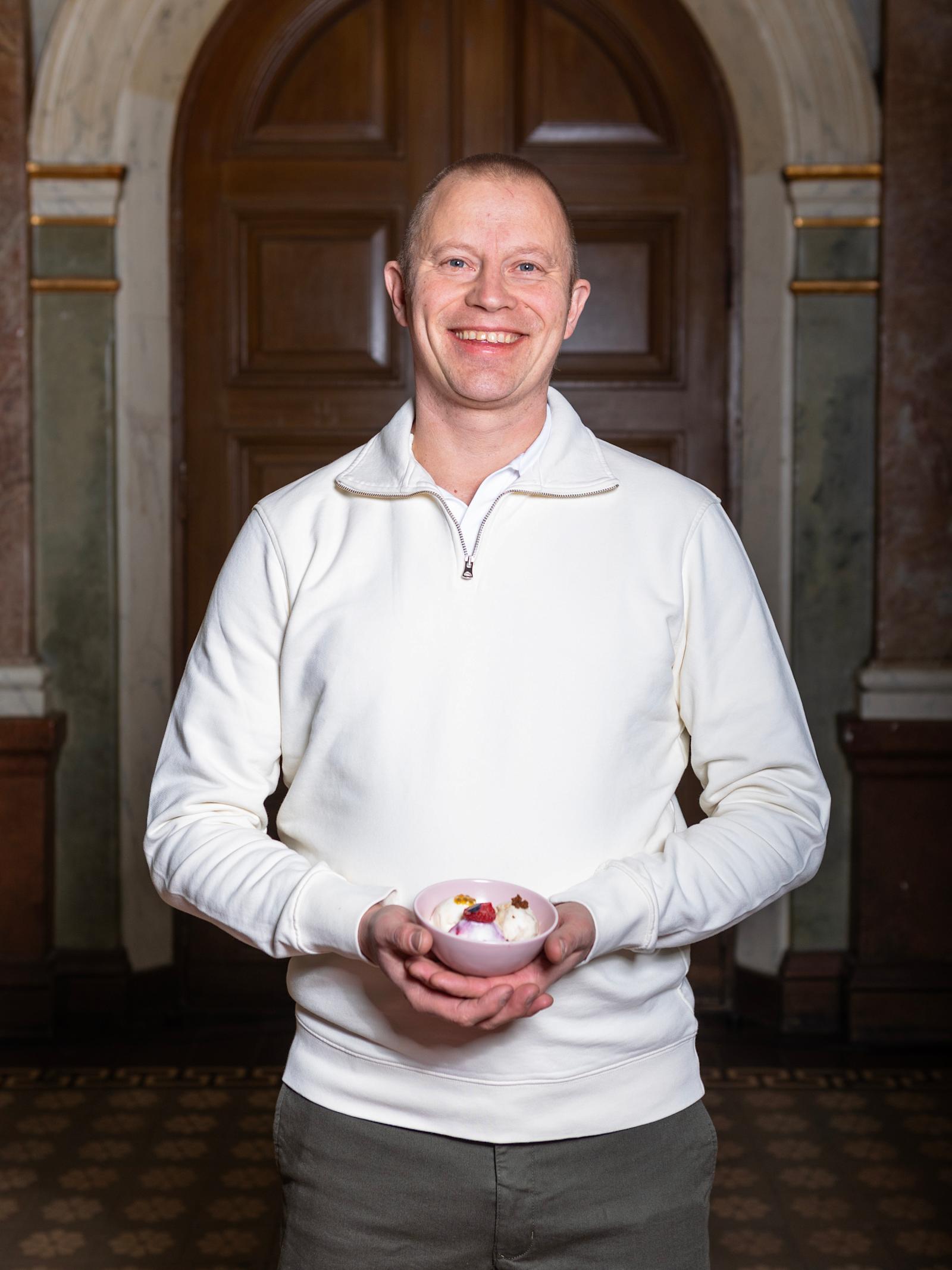 Samuli Wirgentius seisoo ja hymyilee. Kädessä on kuppi jäätelöä.