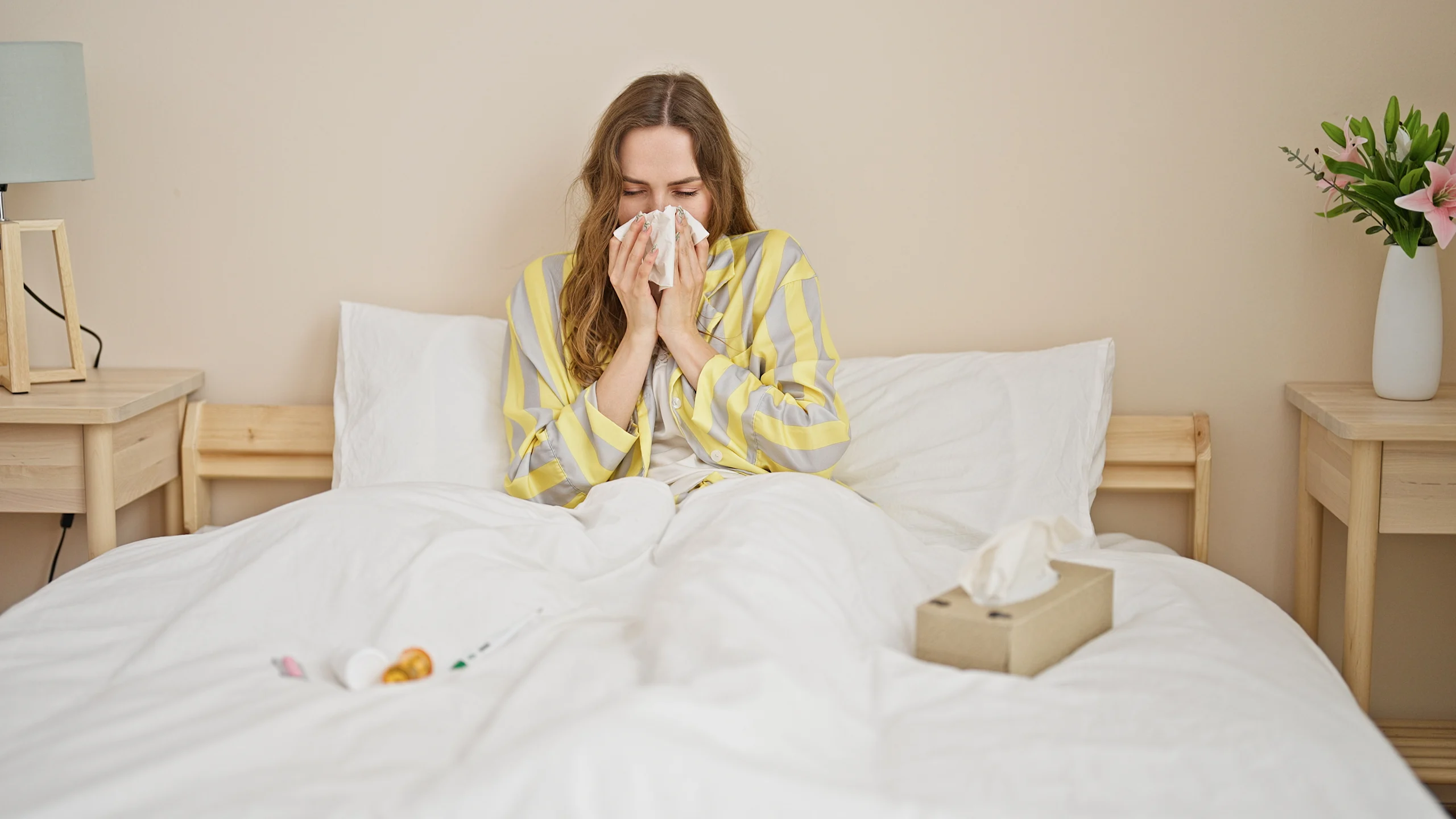 Nainen makaa sängyssä sairaana, niistää nenäänsä